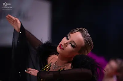 Dancesport competitor: Female dancer: black dramatic costume with sheer sleeves, black feather trim, an