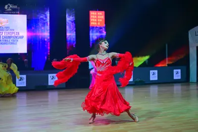 Dancesport competitor: Female dancer in foreground: red ballroom dress with a decorated bodice and larg