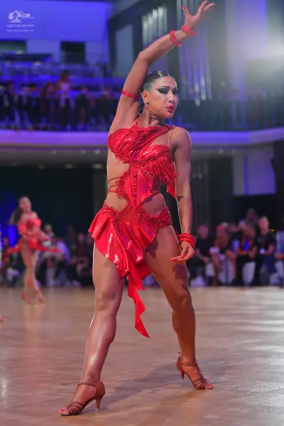 Dancesport competitor: Female dancer in foreground: red latin dress with sequins and cutouts