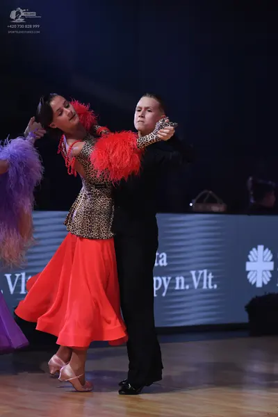 Dancesport competitor: Female dancer: leopard-print bodice with red feather trim and a bright red flowi