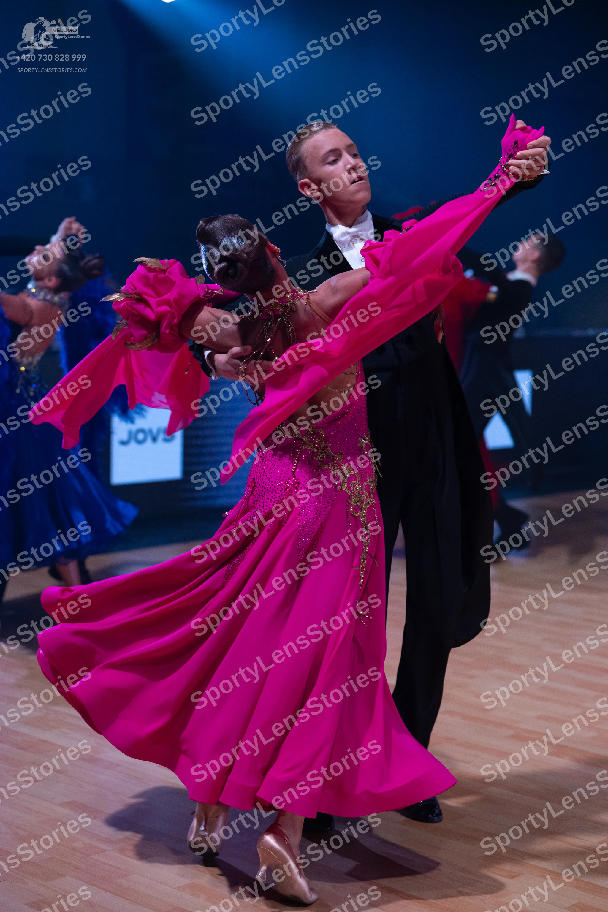 Dancesport competitor: Female dancer in foreground: bright pink ballroom gown with a flowing skirt and