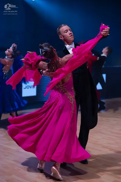 Dancesport competitor: Female dancer in foreground: bright pink ballroom gown with a flowing skirt and 