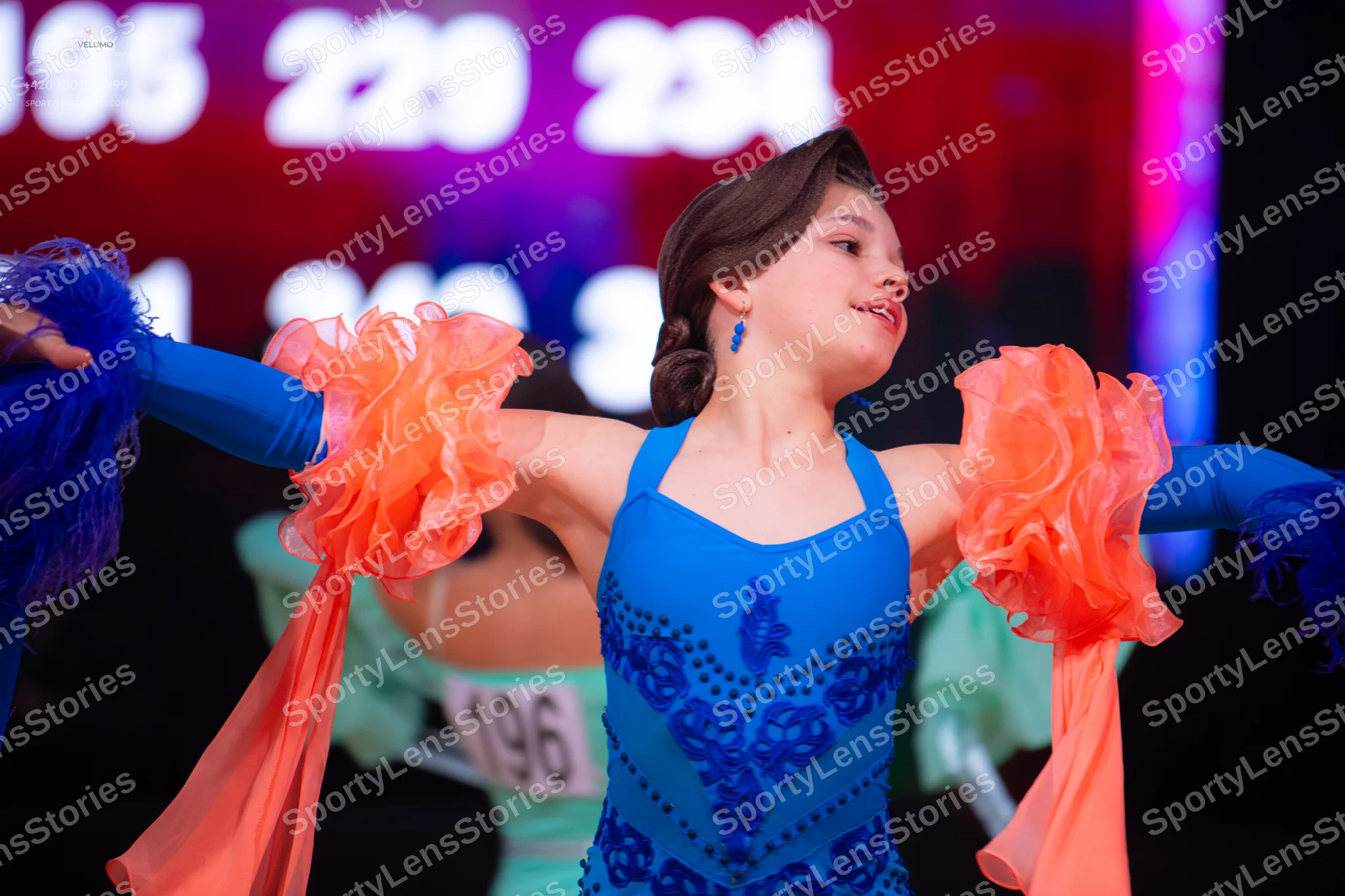 Dancesport competitor: Female dancer (foreground): blue latin dress with dark blue sequin patterns and