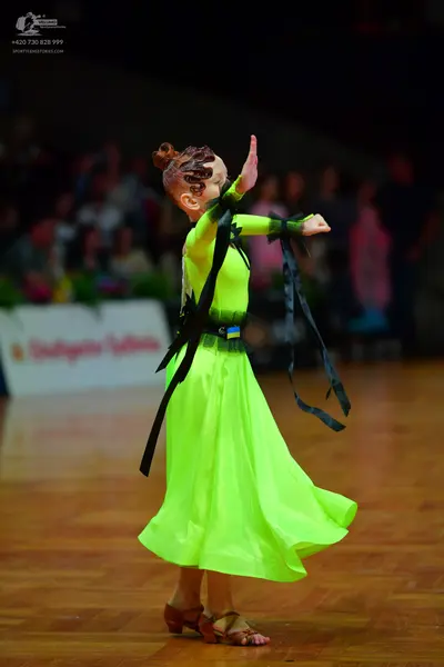 Dancesport competitor: Female dancer: bright lime green ballroom gown with a black waistband and long b