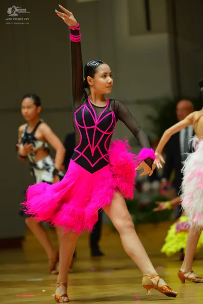 Dancesport competitor: Central female dancer: bright pink Latin dress with a black mesh bodice featurin