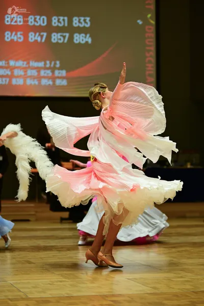Dancesport competitor: Female: pale pink, flowing, voluminous skirt with white overlay