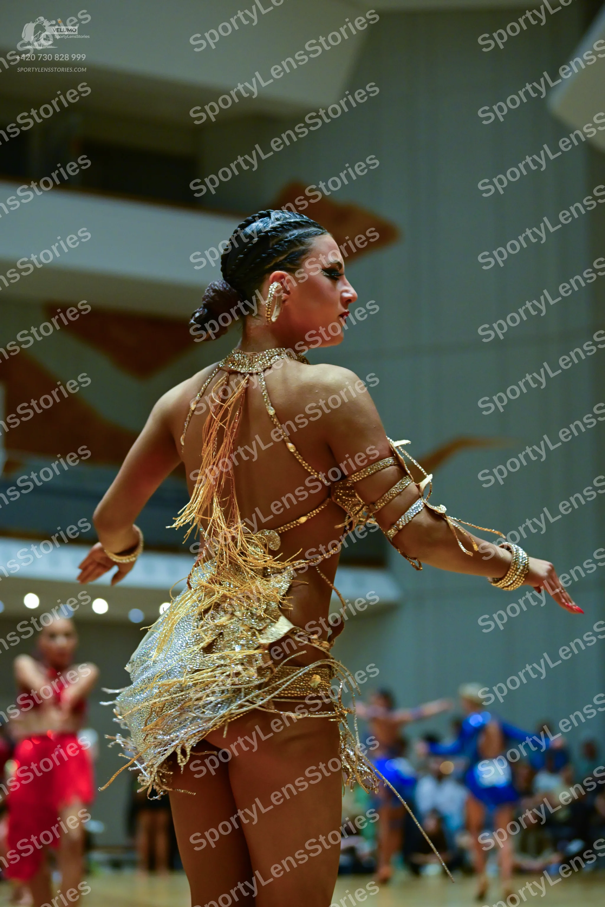 Dancesport competitor: Female dancer in foreground: gold sequined and beaded Latin dance costume with l