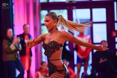 Dancesport competitor: Female dancer: nude-colored Latin dance bodysuit with intricate black and dark g