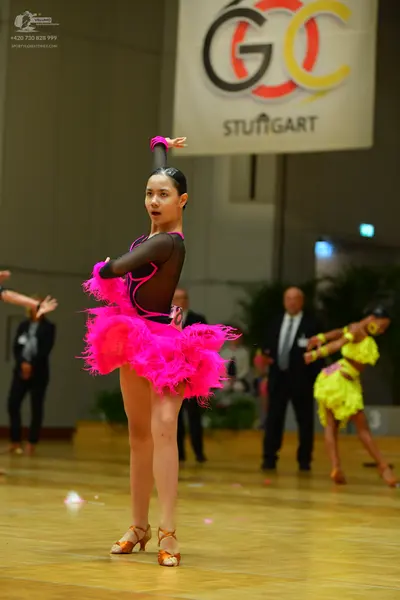 Dancesport competitor: Female dancer in foreground: bright pink Latin dress with a black sheer mesh bod