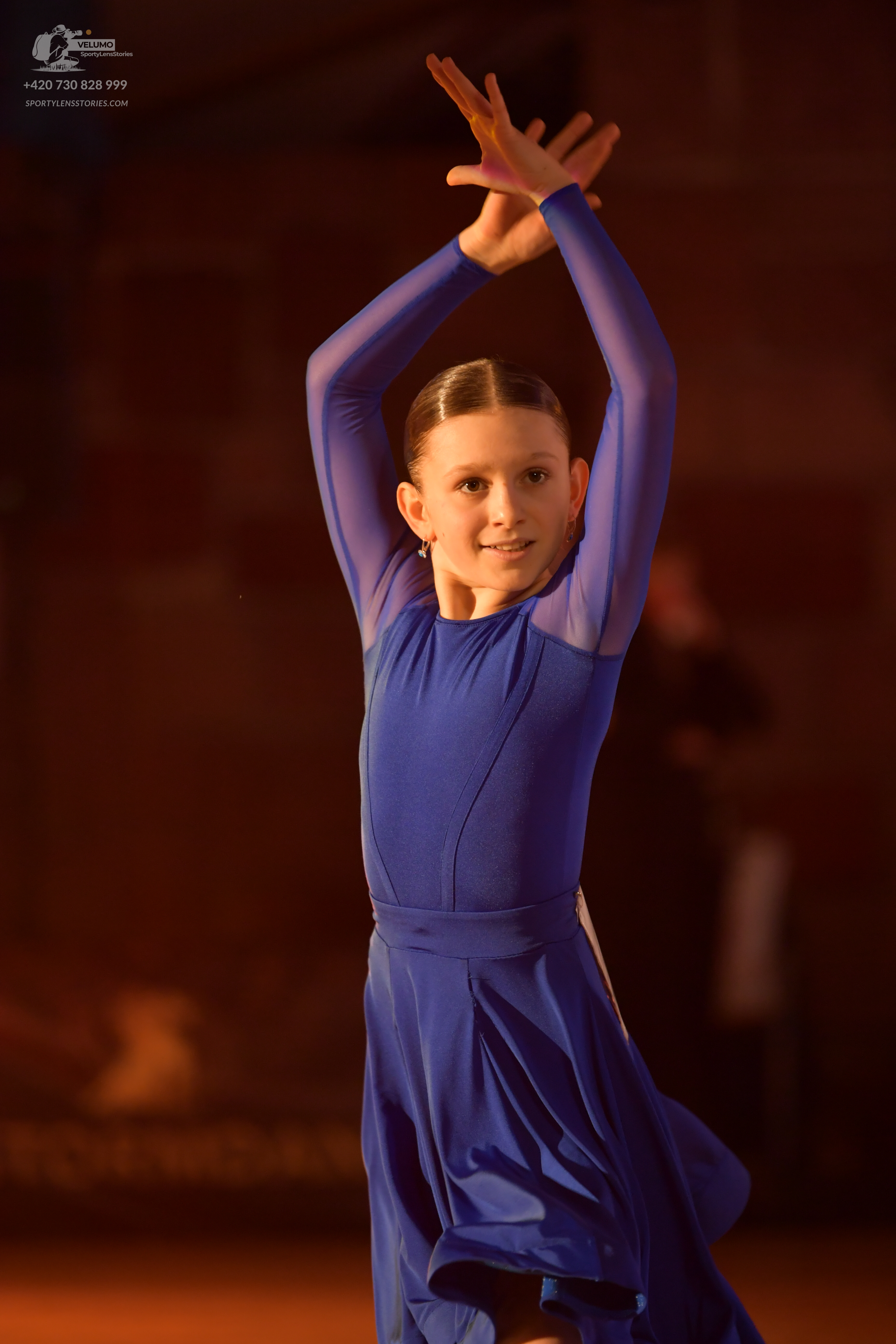 Dancesport competitor: Female dancer: blue long-sleeved dress with mesh detailing on the upper arms and