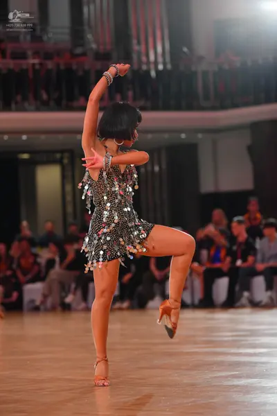 Dancesport competitor: Female dancer: dark-colored Latin dress adorned with numerous shiny sequins or m