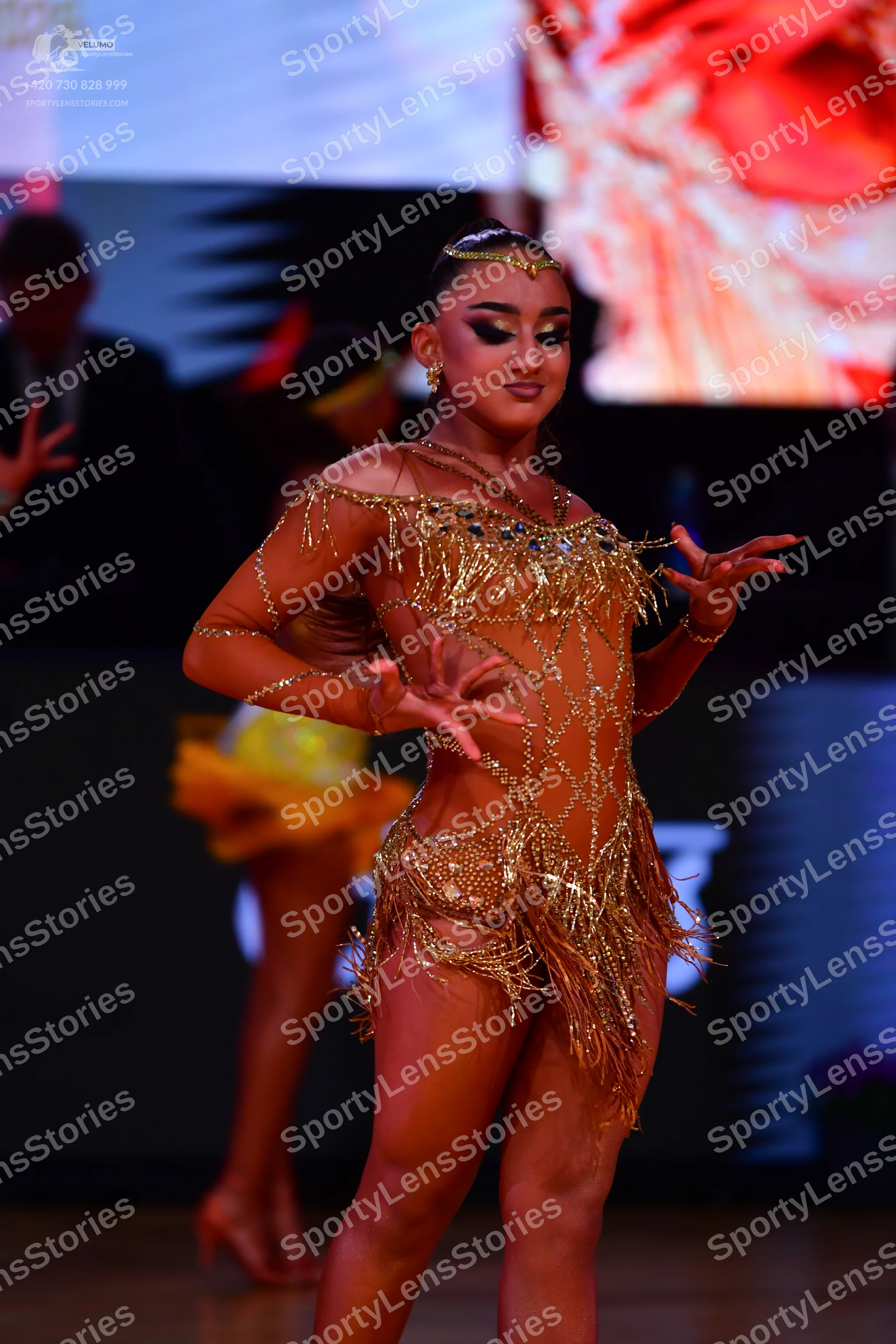 Dancesport competitor: Female dancer in foreground: gold Latin dance costume with sequins, rhinestones,