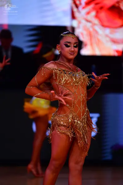 Dancesport competitor: Female dancer in foreground: gold Latin dance costume with sequins, rhinestones,