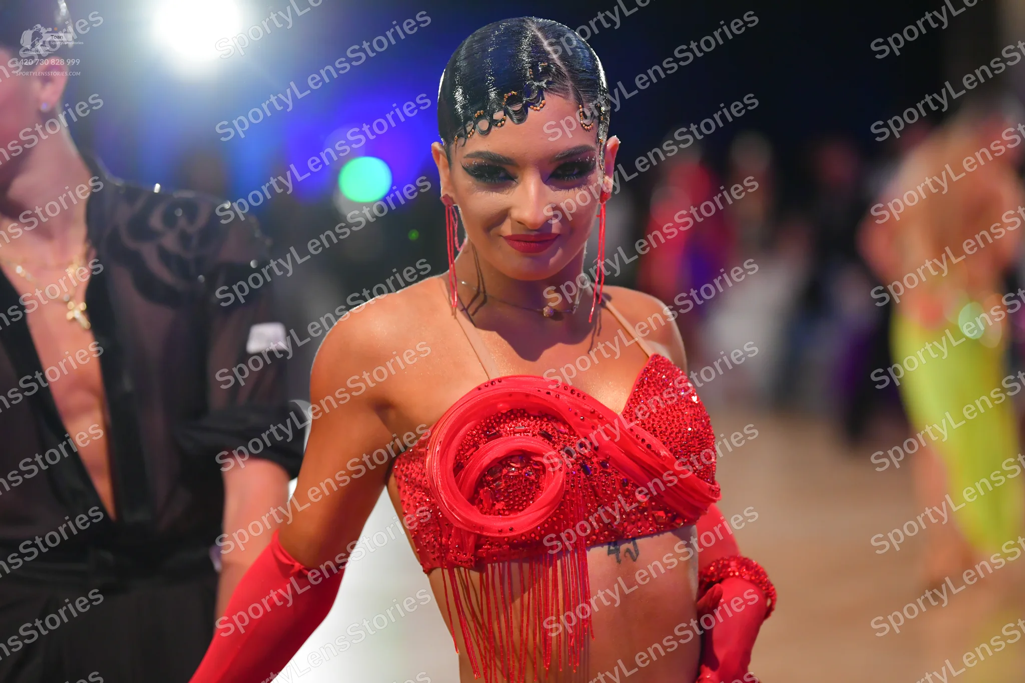 Dancesport competitor: Female dancer: red Latin dress with sequins and long fringe, wearing matching lo