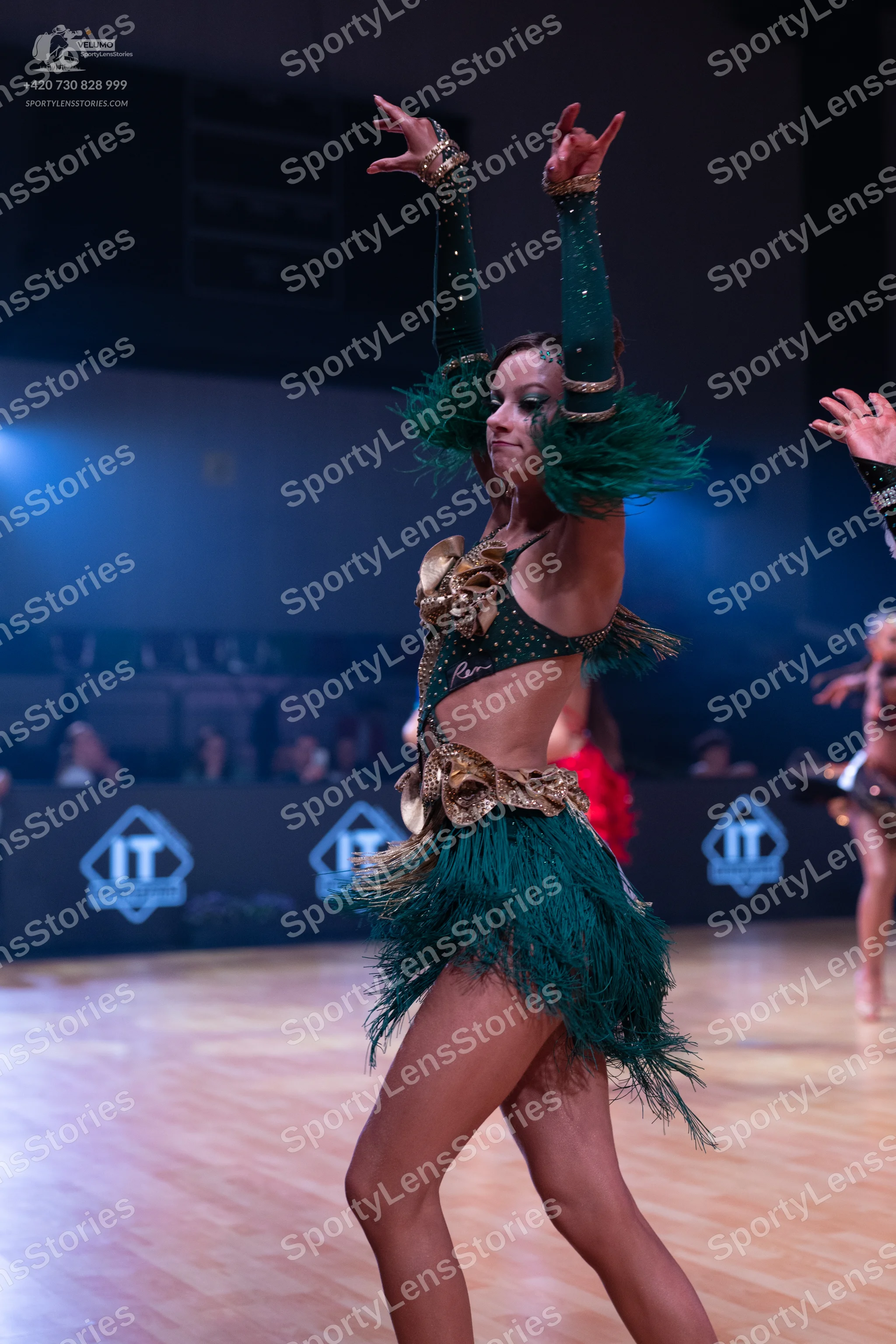 Dancesport competitor: Female dancer in the foreground: emerald green Latin dance dress featuring gold