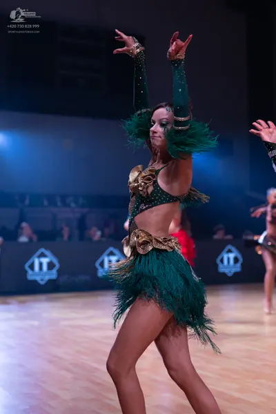 Dancesport competitor: Female dancer in the foreground: emerald green Latin dance dress featuring gold 
