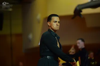 Dancesport competitor: Male dancer: black long-sleeved shirt with a visible white tag on the back