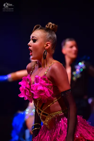 Dancesport competitor: Female dancer: hot pink Latin dance dress featuring large fabric flowers on the 