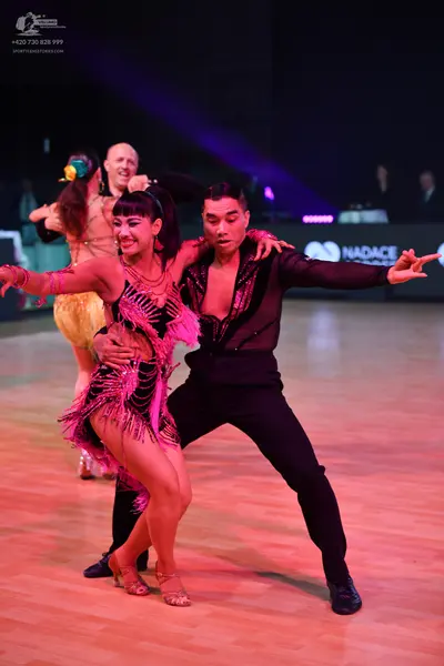 Dancesport competitor: Female dancer in foreground: dark Latin dress with pink/magenta fringe and sequi