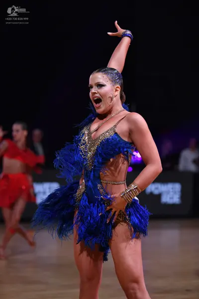 Dancesport competitor: Female dancer in foreground: blue latin costume with blue feathers, gold/silver 