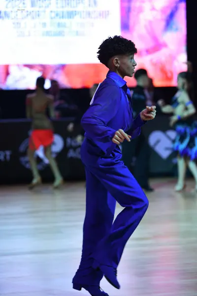Dancesport competitor: Male dancer in foreground: blue long-sleeved shirt and matching blue trousers