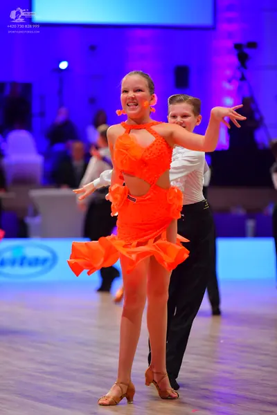 Dancesport competitor: Female dancer: bright orange Latin dance dress with cutouts and a ruffled skirt