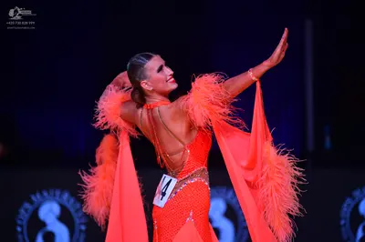 Dancesport competitor: Female dancer: bright orange latin dress with sequins and large feather sleeves