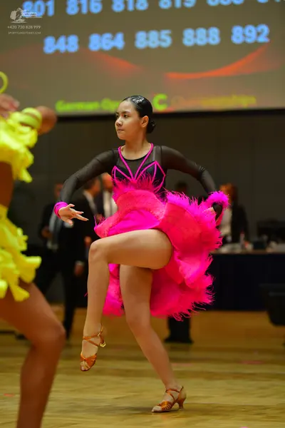 Dancesport competitor: Female dancer in foreground: pink and black Latin dress with a long-sleeved bodi