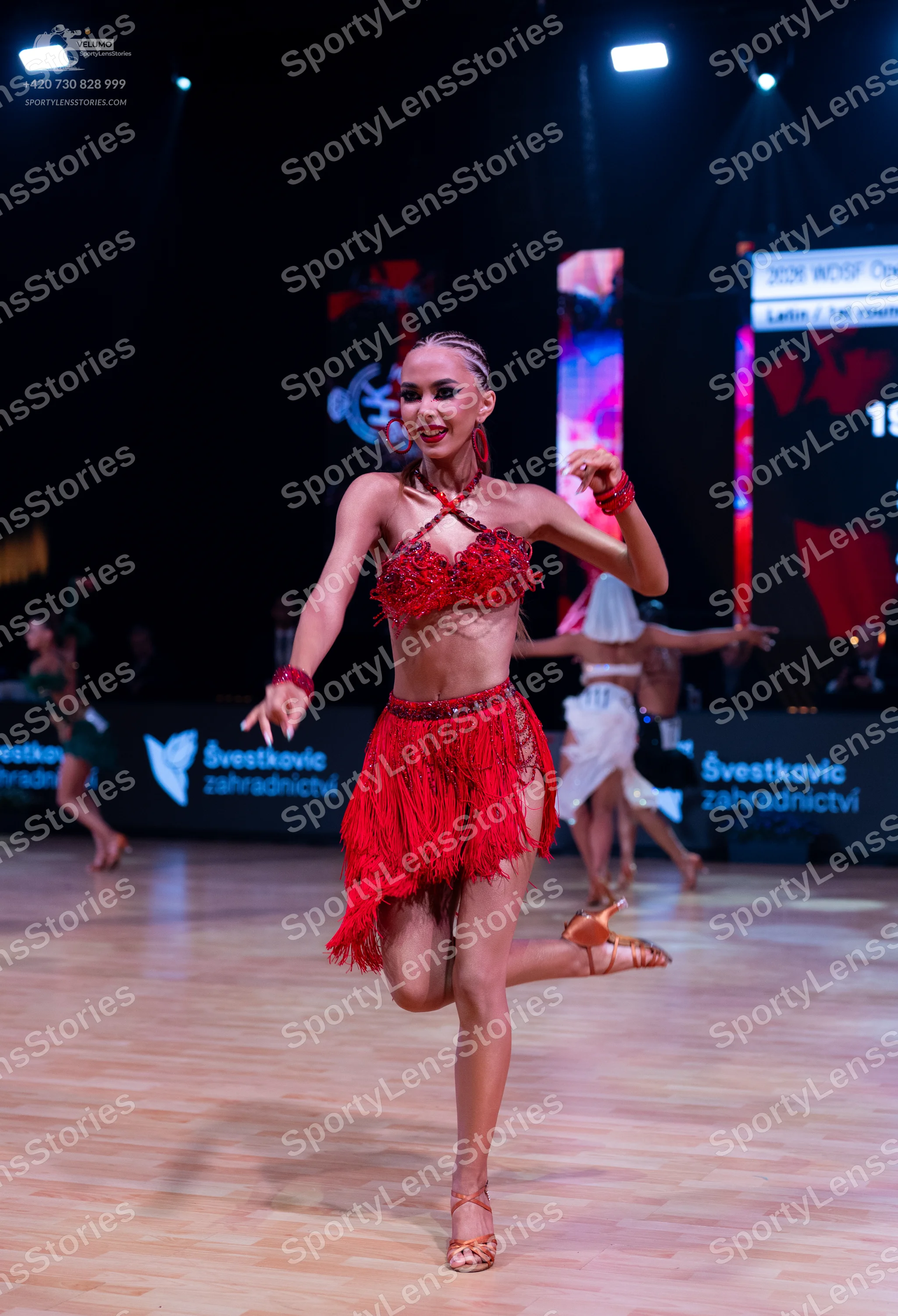 Dancesport competitor: Female dancer (foreground): red latin dress with lace bodice, long fringe skirt,