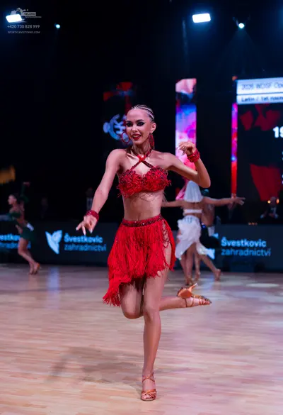 Dancesport competitor: Female dancer (foreground): red latin dress with lace bodice, long fringe skirt,