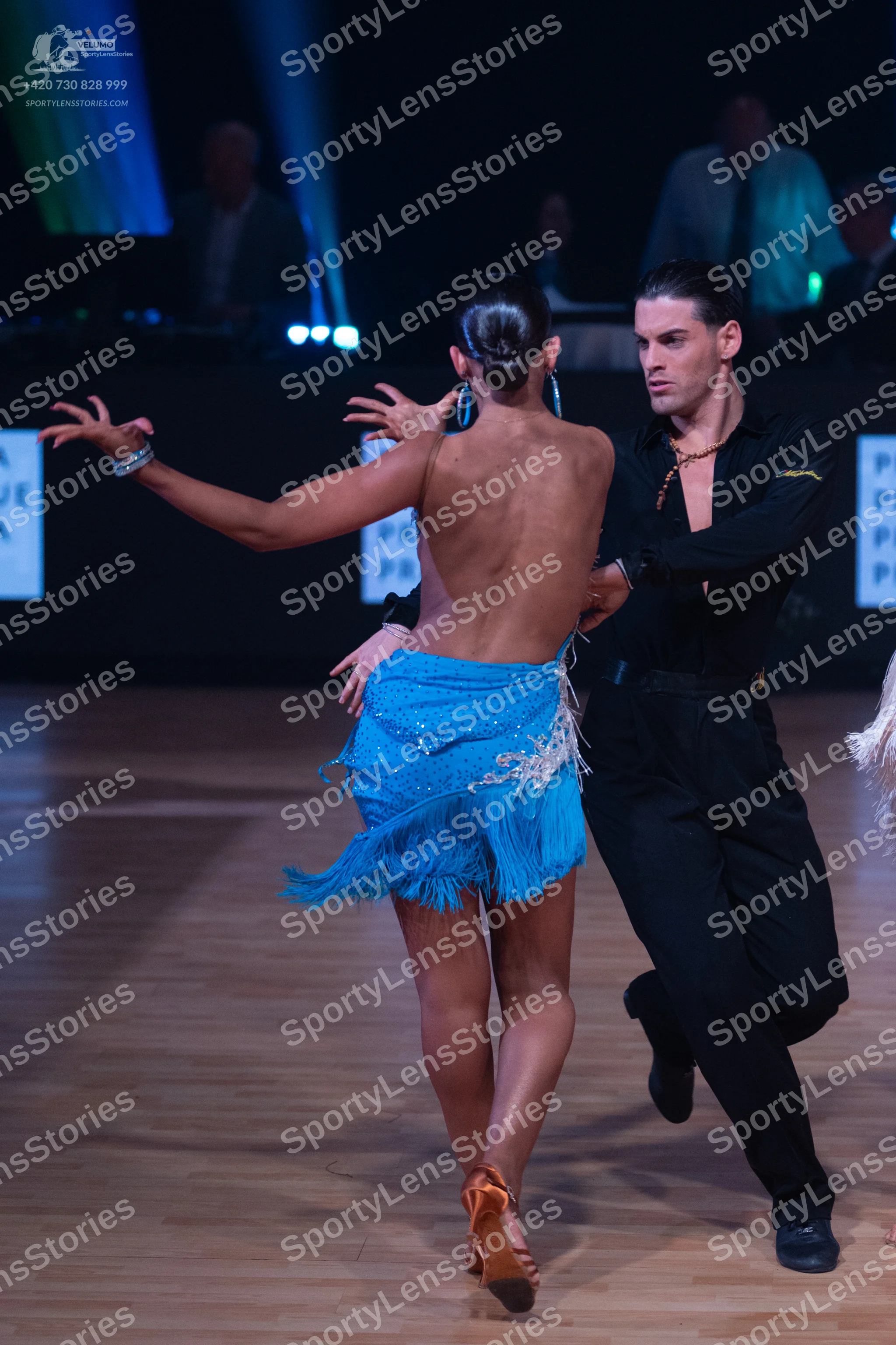 Dancesport competitor: Female dancer: blue Latin dress with sequins and fringe, hoop earrings, and a br