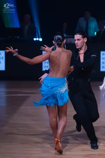 Dancesport competitor: Female dancer: blue Latin dress with sequins and fringe, hoop earrings, and a br