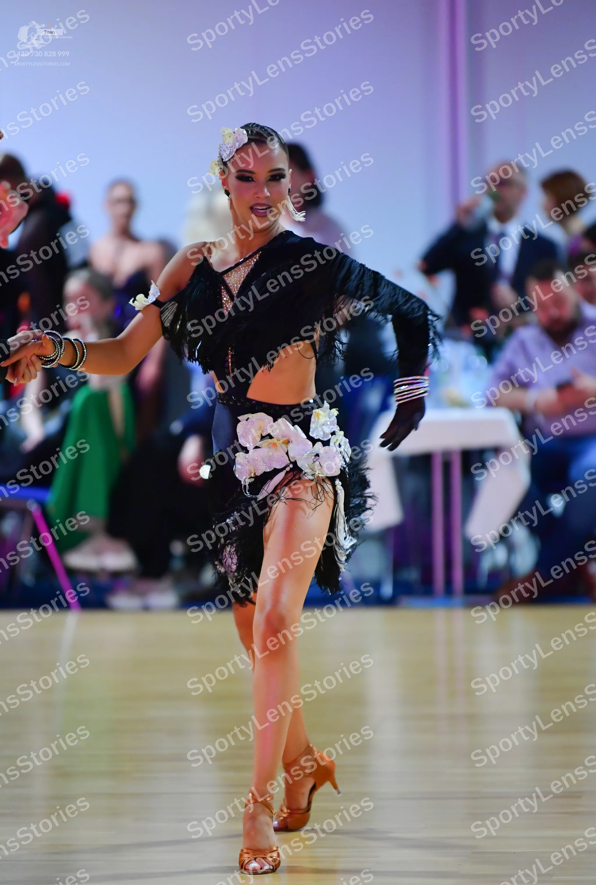 Dancesport competitor: Female dancer: black Latin dance costume with fringe, a cutout top, and large wh