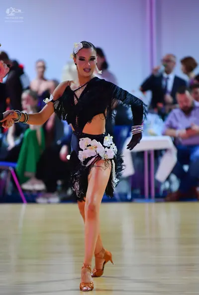 Dancesport competitor: Female dancer: black Latin dance costume with fringe, a cutout top, and large wh