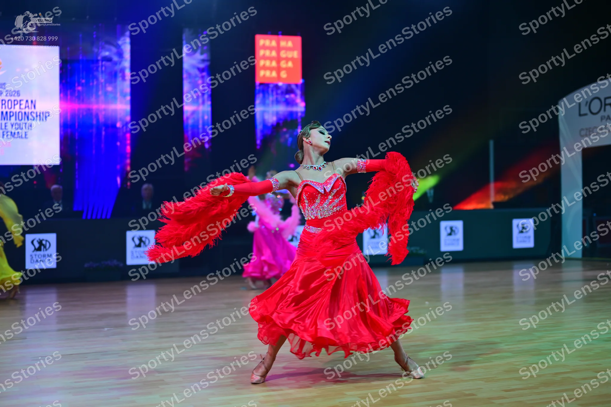 Dancesport competitor: Female dancer in foreground: red Latin dress with voluminous ruffled sleeves and