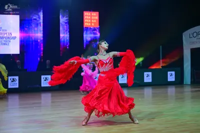 Dancesport competitor: Female dancer in foreground: red Latin dress with voluminous ruffled sleeves and