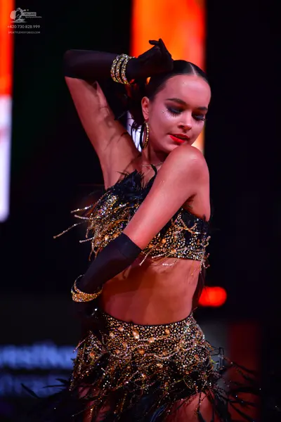 Dancesport competitor: Female dancer: black and gold latin costume consisting of a heavily embellished 