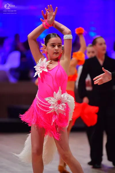 Dancesport competitor: Female dancer 1: bright pink latin dress with long fringe, large white floral em