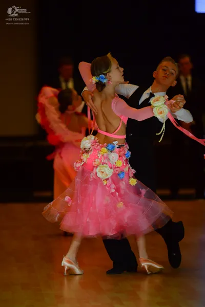Dancesport competitor: Female dancer: pink latin dress with long sheer sleeves, a pink band around the 