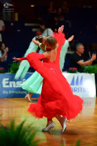 Dancesport competitor: Female dancer in foreground: red latin dress with fringe