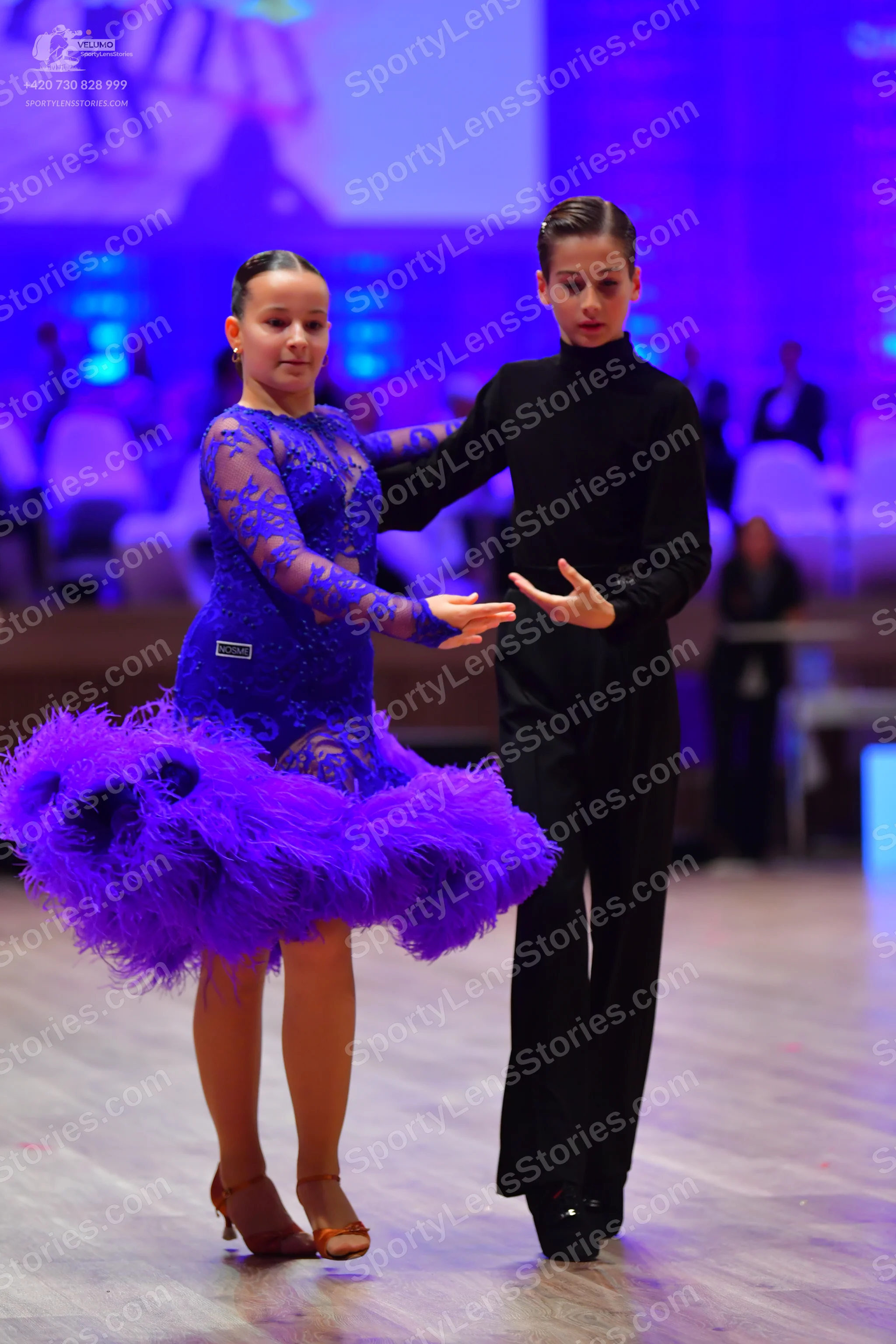 Dancesport competitor: Female dancer: royal blue lace long-sleeved dress with a voluminous, feathered p