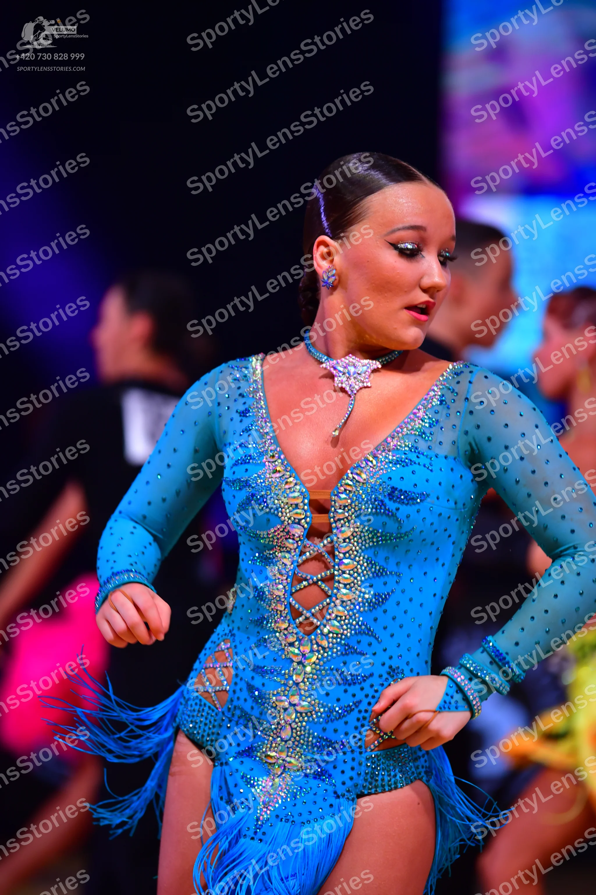 Dancesport competitor: Female dancer: bright blue long-sleeved Latin dance dress heavily embellished wi