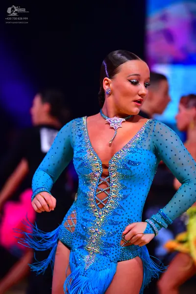 Dancesport competitor: Female dancer: bright blue long-sleeved Latin dance dress heavily embellished wi