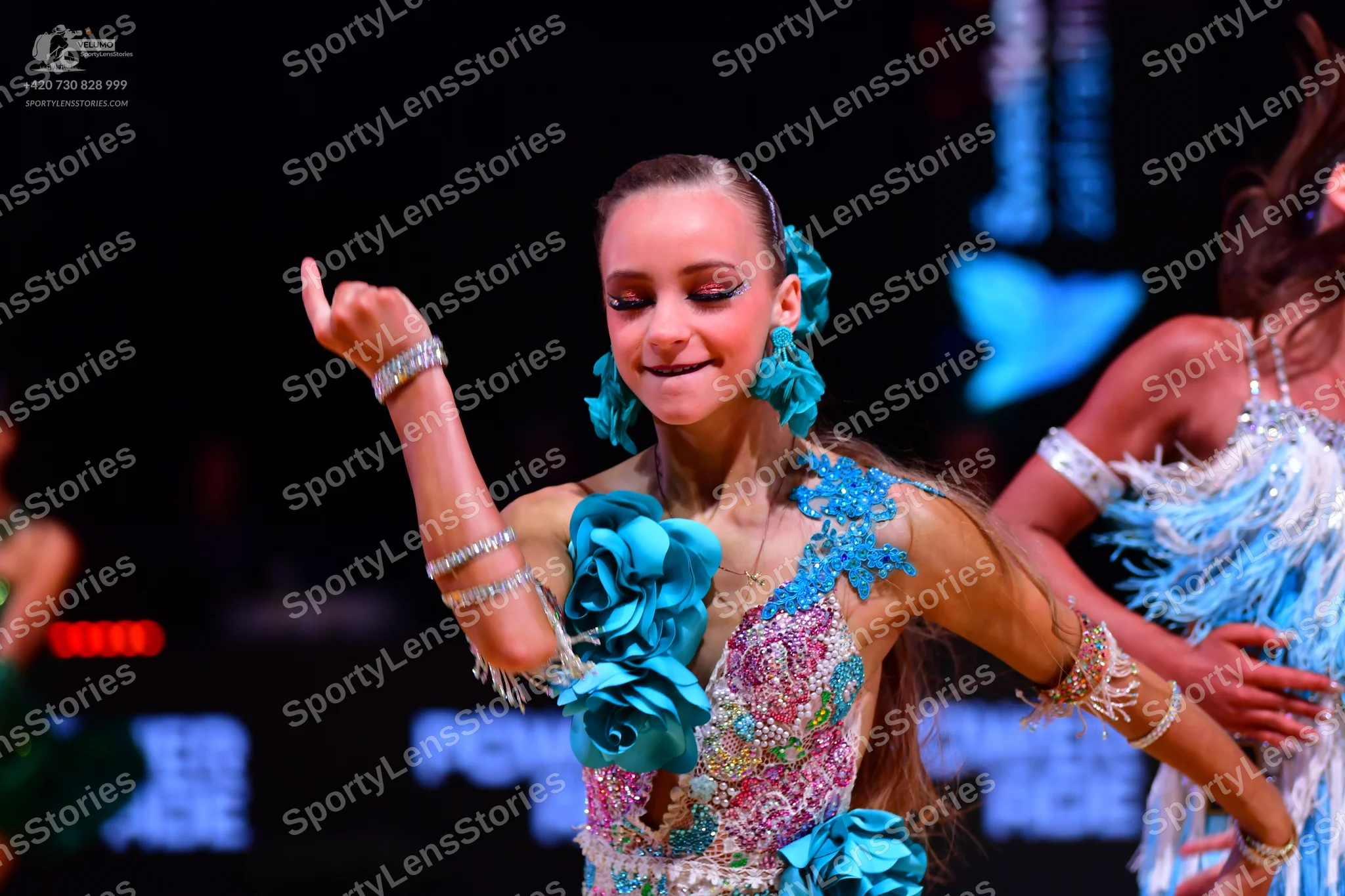 Dancesport competitor: Female dancer in center: turquoise and pink latin dress with large 3D turquoise