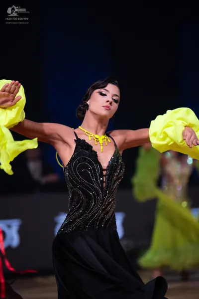 Dancesport competitor: Female dancer in foreground: black Latin dance dress with a sequined bodice feat