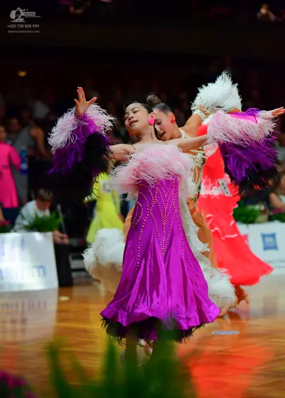 Dancesport competitor: Female dancer 1: purple satin Latin dress with large white, pink, and dark purpl
