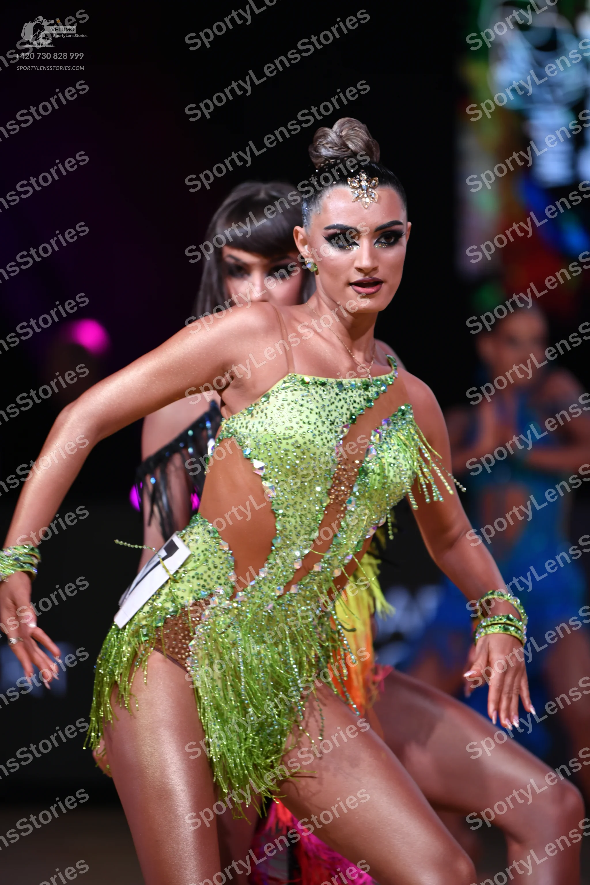 Dancesport competitor: Female dancer in foreground: lime green Latin dance dress with sequins, cutouts,