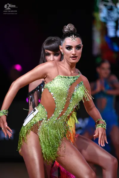 Dancesport competitor: Female dancer in foreground: lime green Latin dance dress with sequins, cutouts,