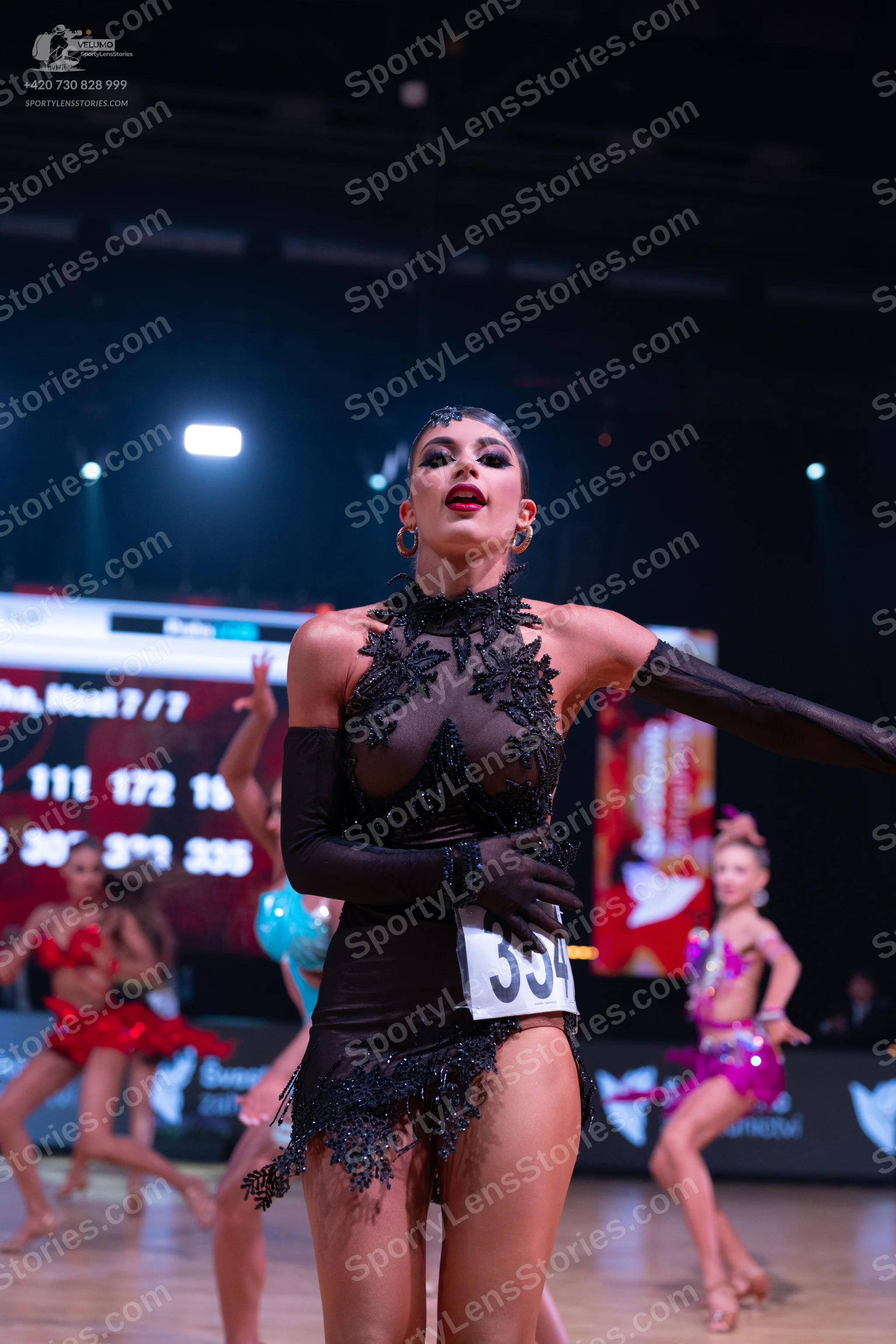 Dancesport competitor: ** Black, form-fitting latin dress with a high neckline and a dramatic, embellis