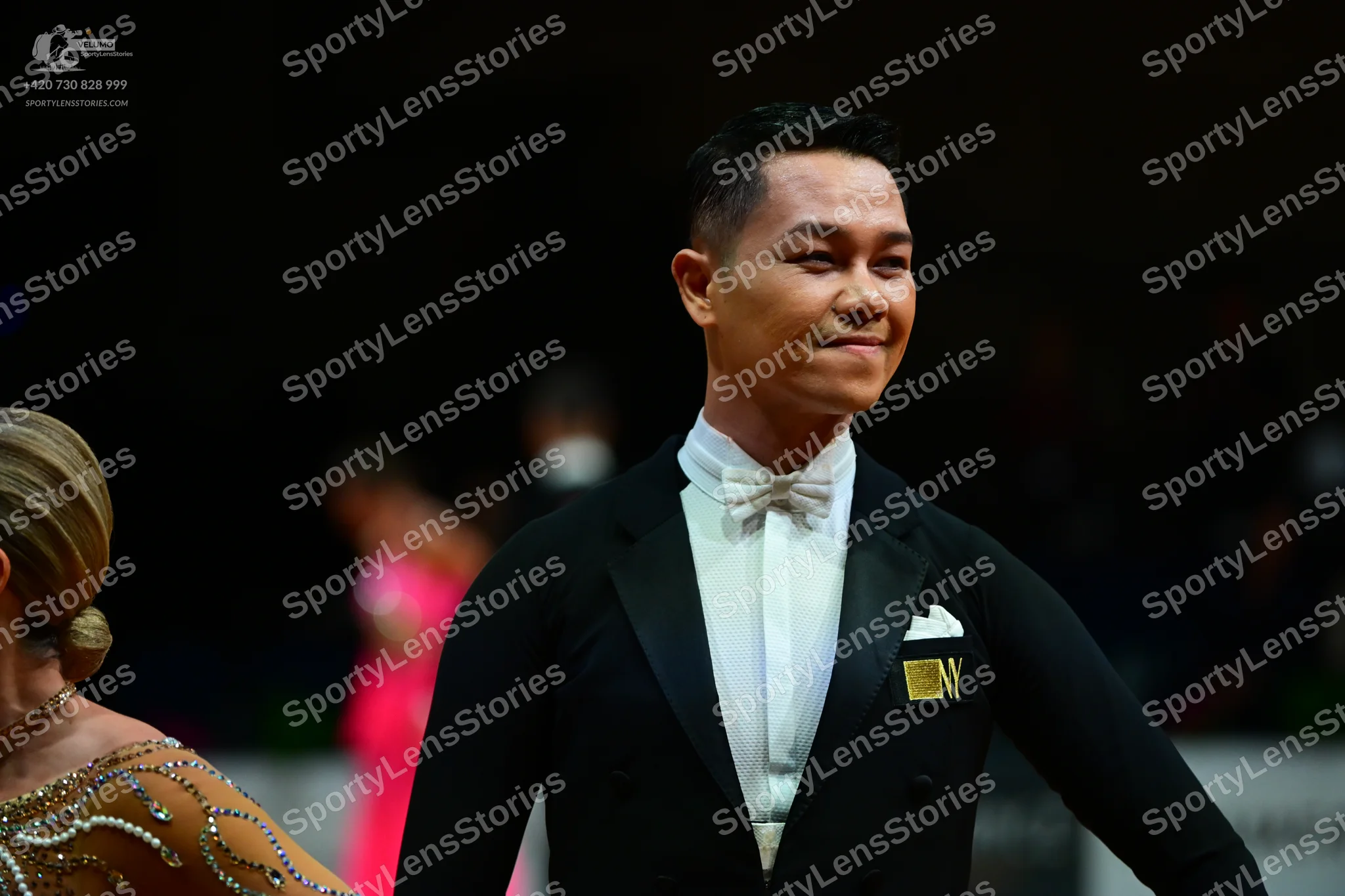 Dancesport competitor: Male dancer: black tuxedo with a white shirt, white bow tie, and white pocket sq